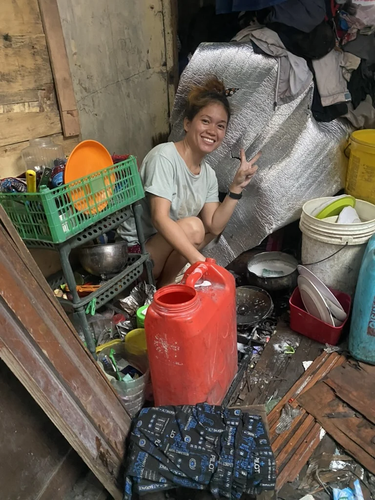 A woman beside pans, buckets and household supplies in a compact space.
