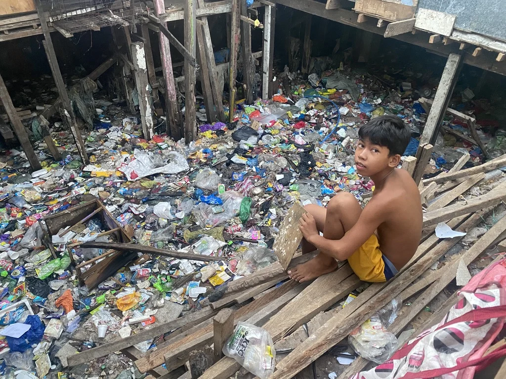 A person sitting on wooden planks beside an area filled with discarded materials.